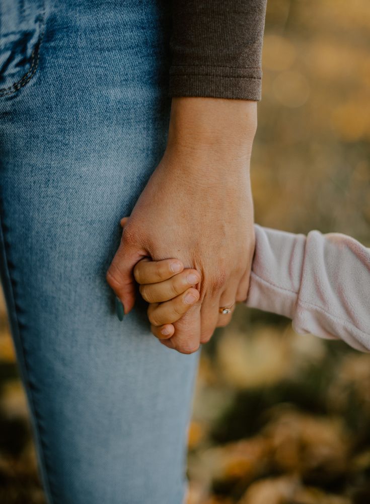 Volwassen hand die de hand van een kind vasthoudt in het najaarslicht